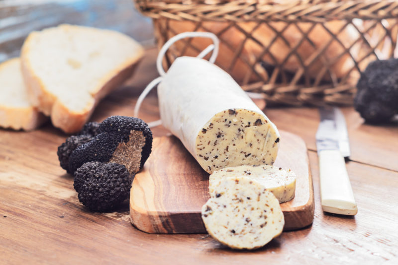 A tube of truffle butter next to black truffles and sliced bread