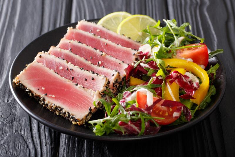 A black plate that contains cooked vegetables and sliced limes