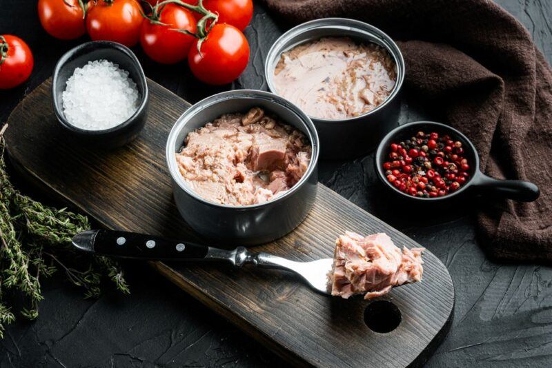 Two cans of tuna that have been opened, next to small containers of salt and pepper, along with fresh tomatoes. There's also a fork with more tuna on it.