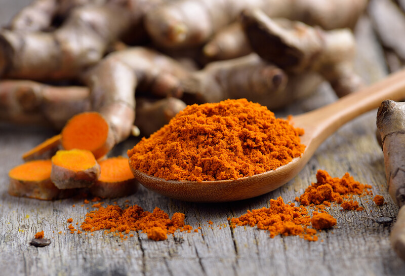 a wooden ladle full of turmeric powder with freshly cut and whole turmeric roots and loose turmeric powder around it.