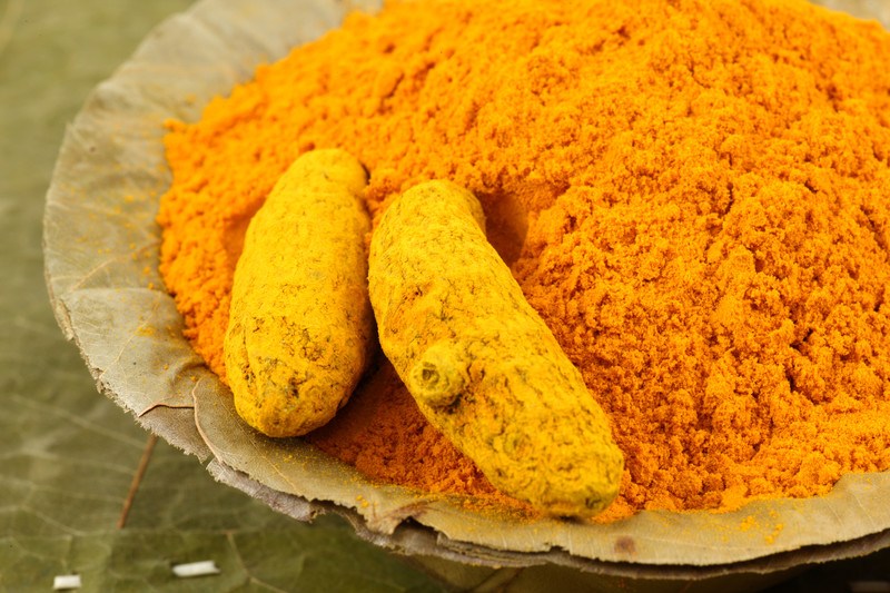 This photo shows two pieces of turmeric in a pile of orange turmeric powder on green leaves.