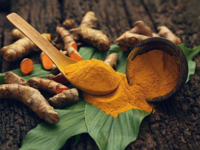 Turmeric roots, turmeric powder, a spoon and a leaf on a table