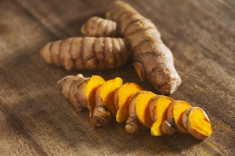 This photo shows a sliced turmeric root next to an uncut turmeric root on a wooden table.