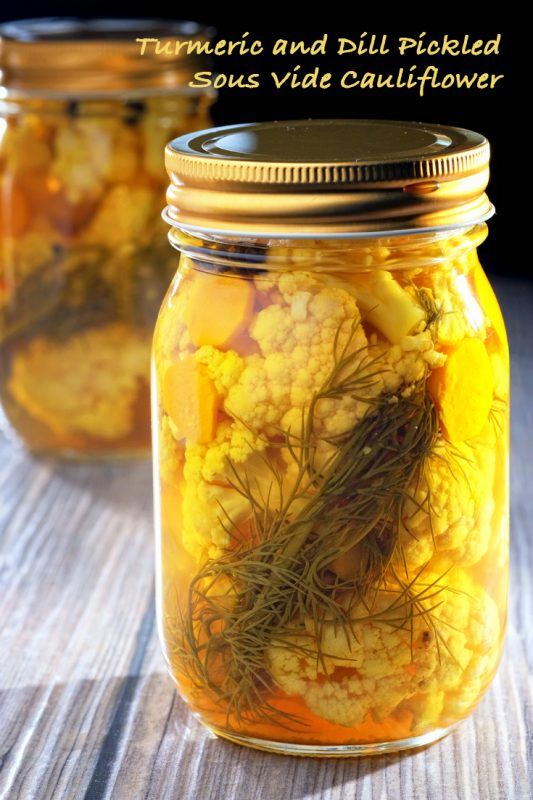 A jar containing turmeric and dill pickled cauliflower, where the different ingredients can be clearly seen. There is a second similar jar in the background.