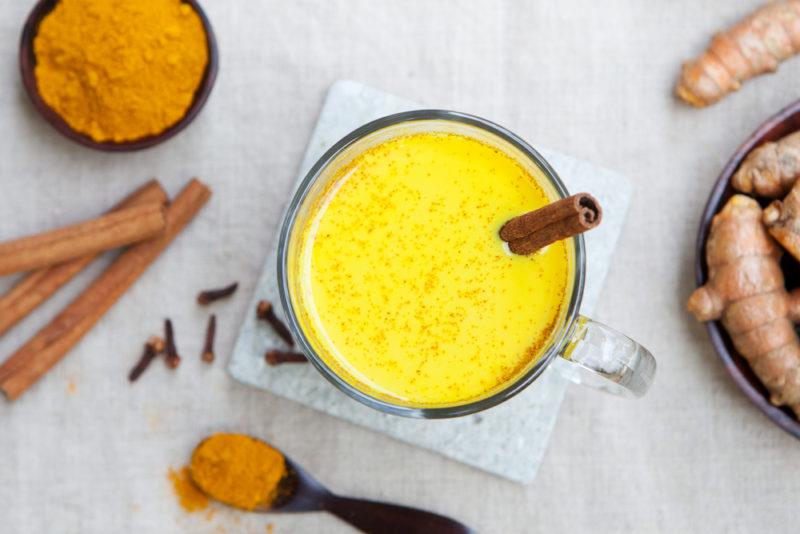 A top down image of a turmeric latte with cinnamon, cloves and turmeric scattered around