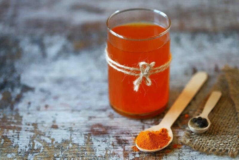 A glass of turmeric and water, next to a spoonful of turmeric powder and one of black pepper