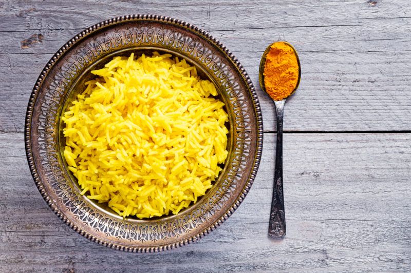 Yellow rice next to a spoonful of turmeric