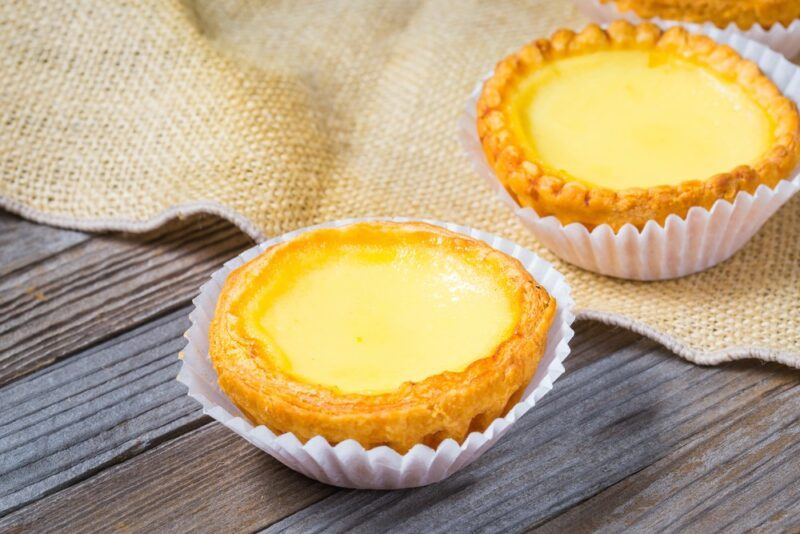 A wooden table with a Chinese egg tart in foil, next to a cloth with a second tart