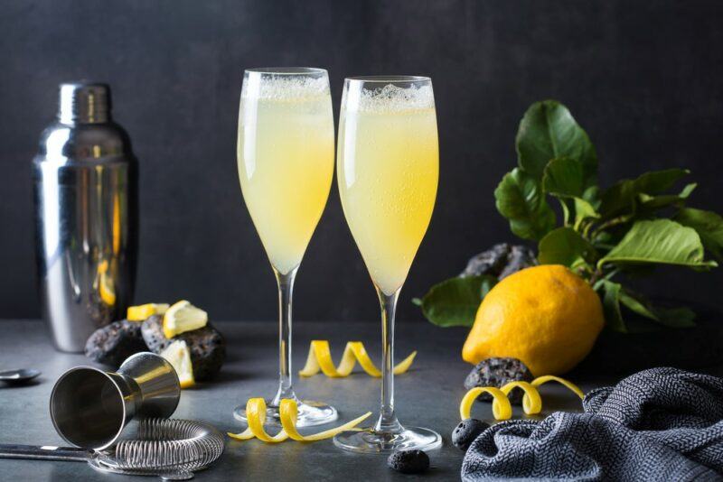 Two French 75 cocktails in champagne glasses, next to a lemon and a cocktail jigger