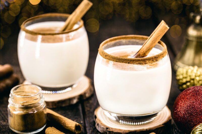 Two glasses of a Long Island coquito cocktail with a cinnamon stick as a garnish