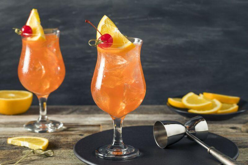 Two hurricane glasses containing Singapore sling cocktails against a gray wall