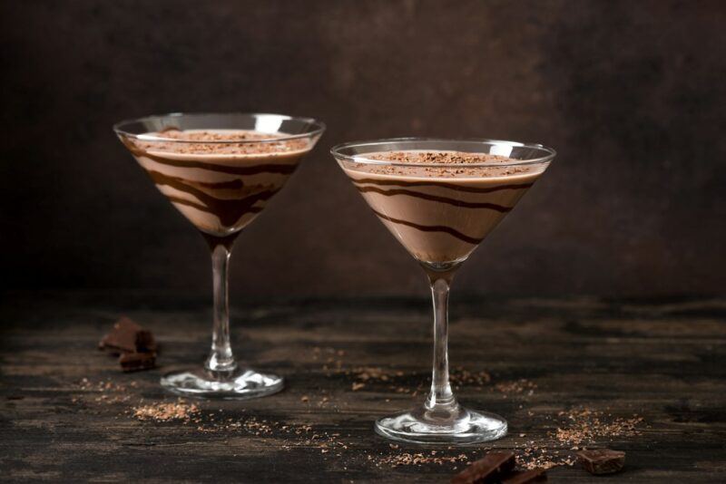 A wooden table with two Toblerone cocktails, each with chocolate syrup around the edge of the glass