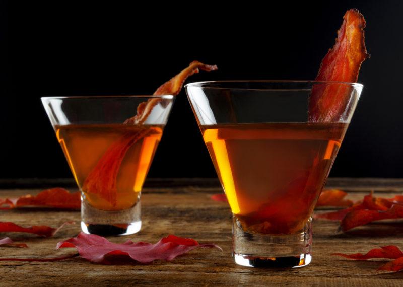 Two whiskey cocktails with bacon as a garnish