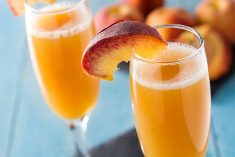 Two champagne glasses containing bellinis, each garnished with a peach wedge