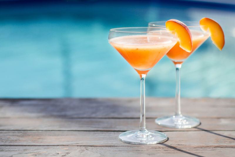 Two bellini cocktails next to the poolside garnished with a peach wedge