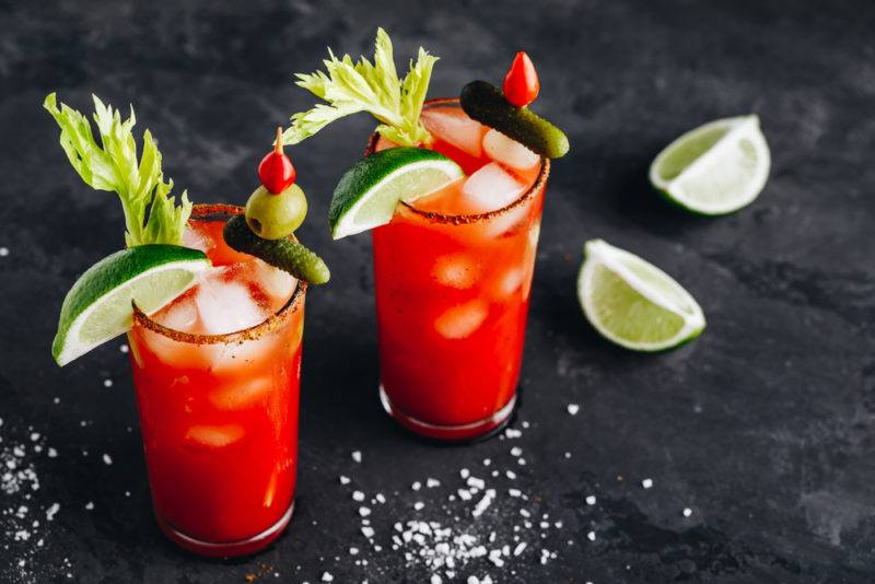 Two bloody Mary cocktails with various savory garnishes and wedges of lime