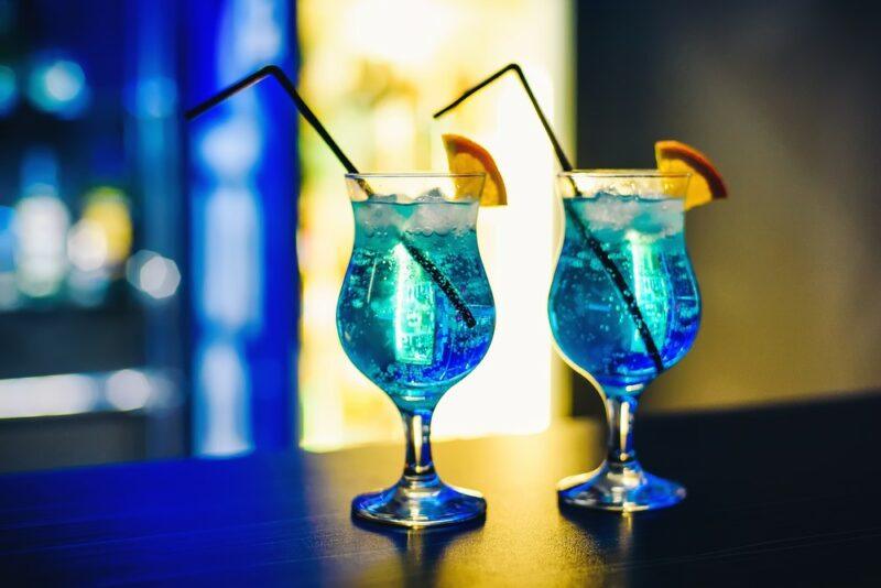 Two blue curacao cocktails sitting on a bar with citrus wedges and straws