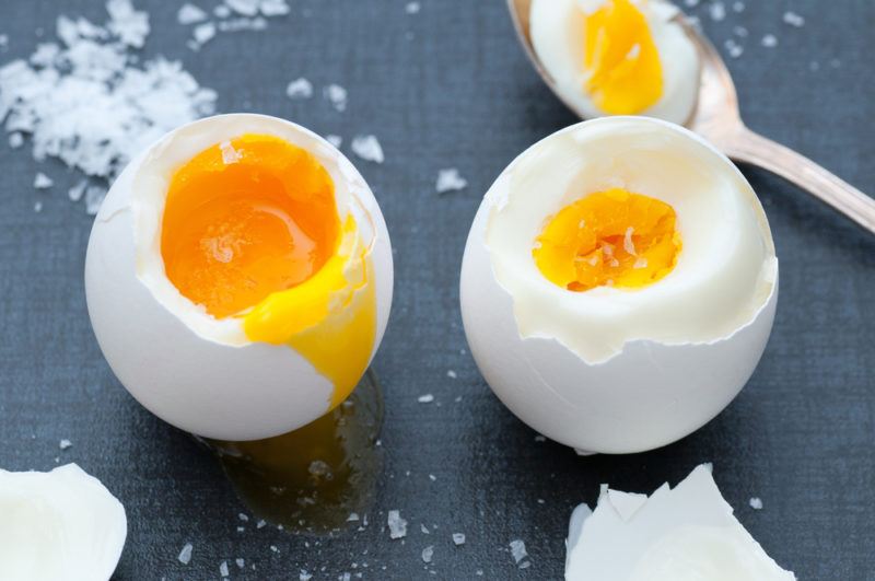 Two boiled eggs on a black background with a spoon and salt