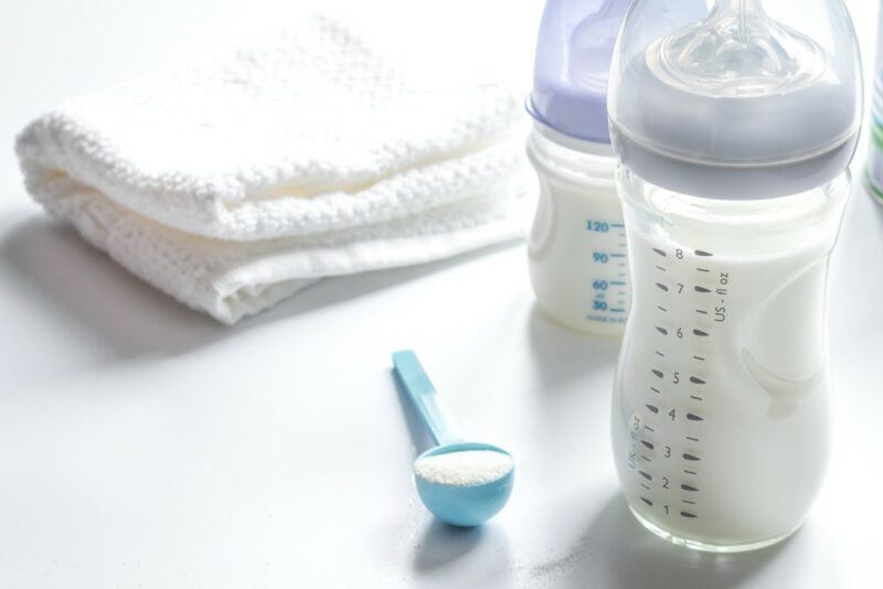 Two bottles of baby formula, next to cloth nappies, and a scoop of the powder