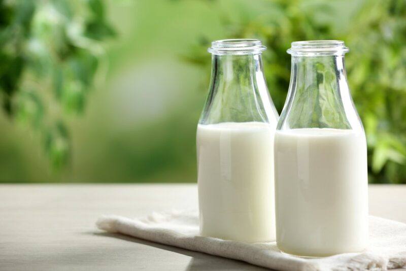 Two bottles of milk sitting on a cloth on a table, with an out of focus green backdrop