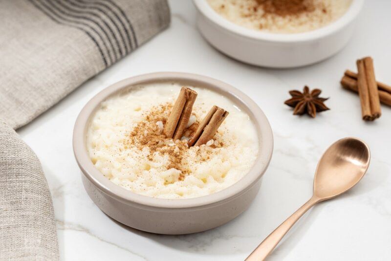 Two gray bowls of arroz con leche on a table, with cinnamon as a topping. There is also a spoon, some cinnamon, and some star anise on the table