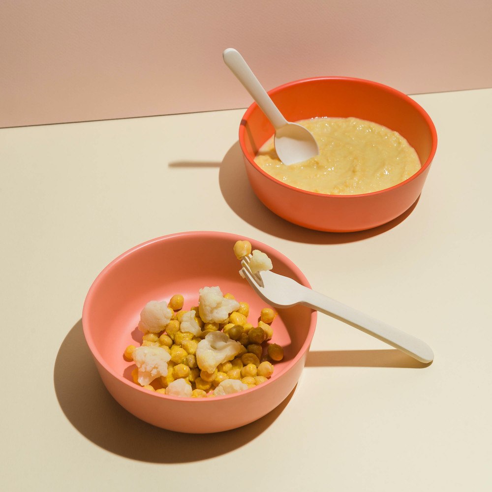 Two orange bowls sitting on an off-white table with baby food