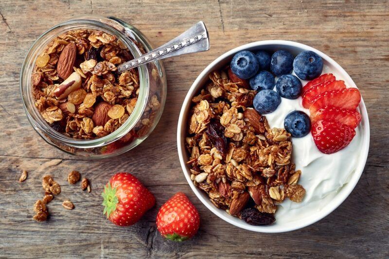 A large bowl of granola with berries and yogurt, next to a jar of granola