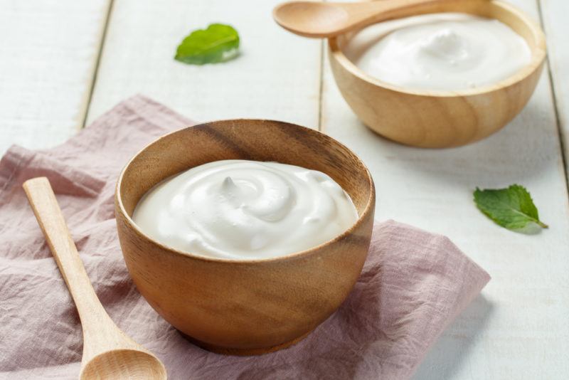 Two wooden bowls that contain yogurt on a light table with a spoon