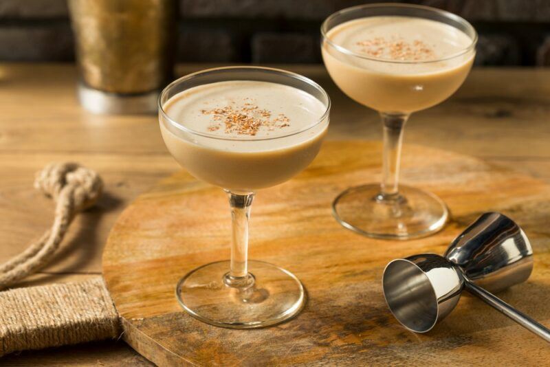 Two brandy Alexander cocktails on a table, next to a cocktail jigger