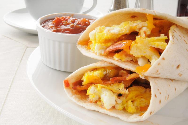 Two breakfast burritos next to some sauce | Food For Net Two breakfast burritos on a white plate next to a small white bowl of sauce