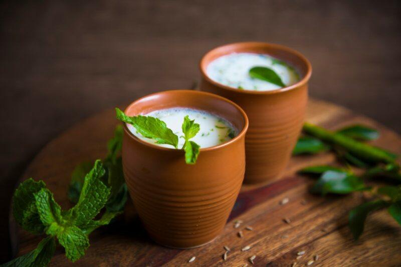 Two brown mugs filled with buttermilk, with some green leaves on top