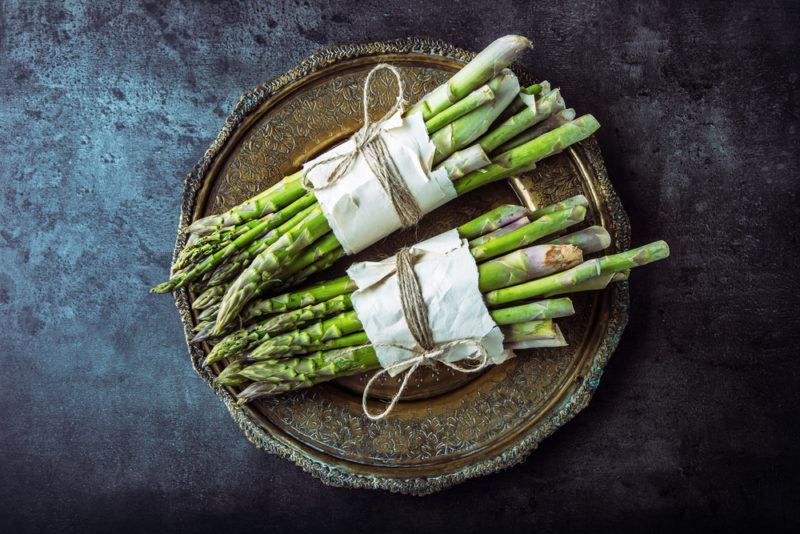 Two bundles of asparagus on a round wooden board. Each bundle is wrapped in paper and tied with string