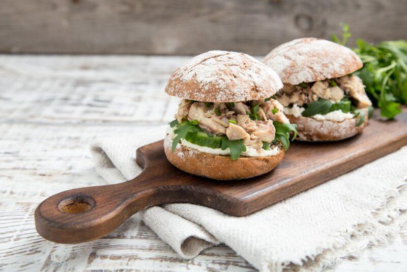 Two homemade burgers on a wooden board, each containing spinach and tuna