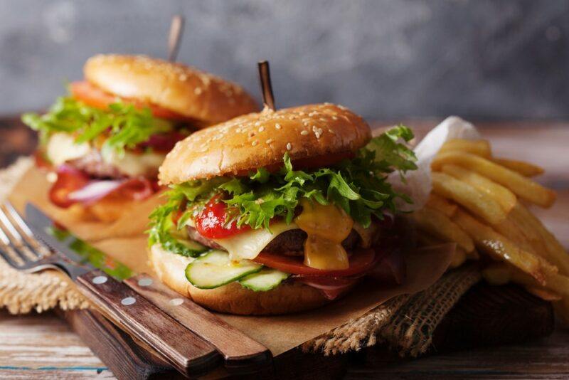 A wooden board with two large burgers, fries, a knife, and a fork