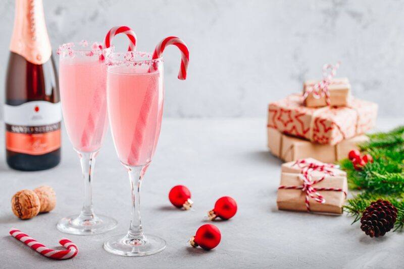 Two champagne glasses with peppermint bark mimosas that are using candy canes as a garnish. There is a bottle of sparkling wine and some presents in the background.