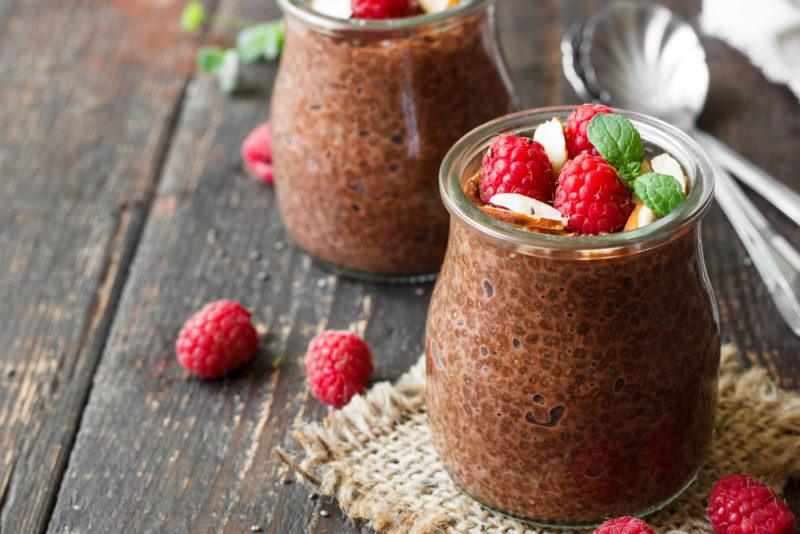 Two glass jars containing chocolate chia pudding, with raspberries on the top