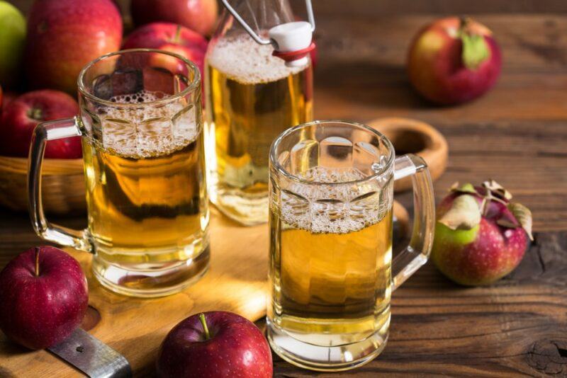 Two cocktails called angry balls, with a bottle of hard apple cider and various fresh apples