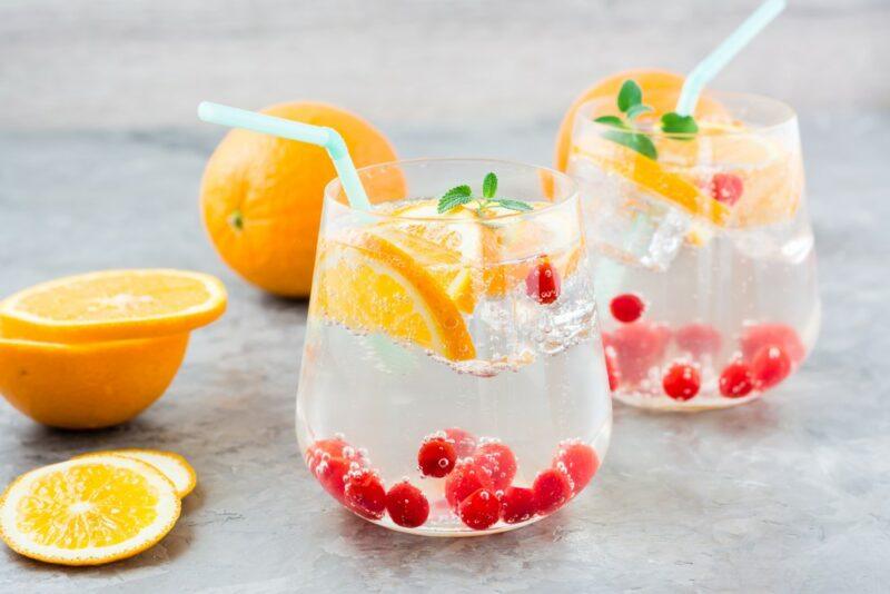 Two glasses containing a simple cocktail made using seltzer water, with orange pieces and cranberrries as a garnish