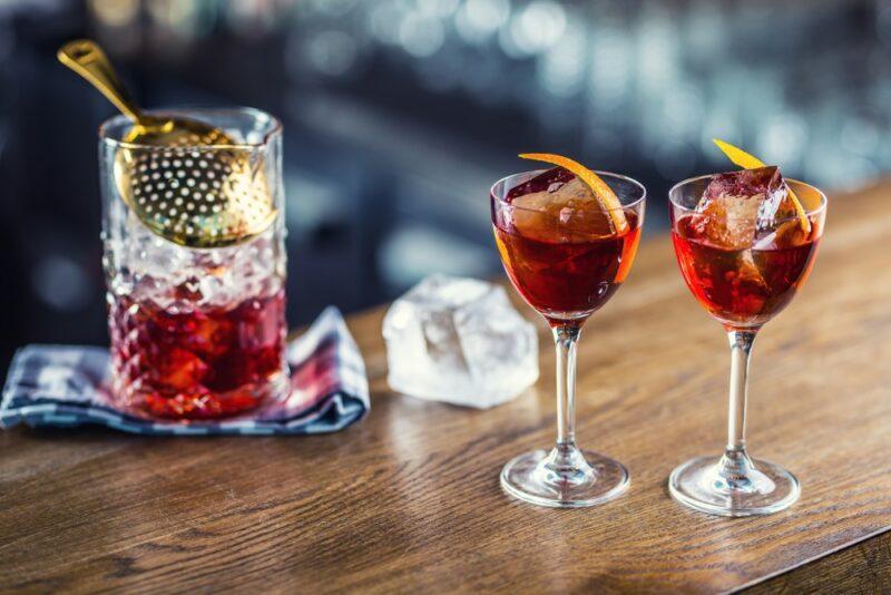 Two glasses containing a conference cocktail on a wooden bar, next to a pitcher of the cocktail