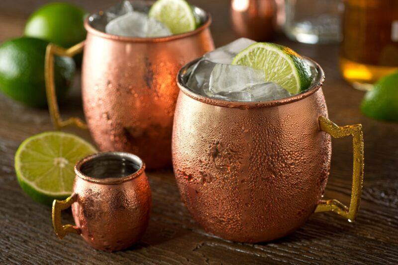 Two copper mugs containing a Mountain Dew Moscow mole cocktail with ice and lime, next to a smaller copper mug