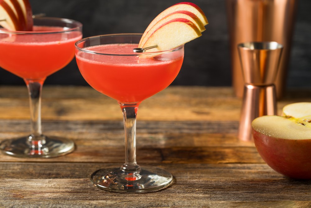 Two coupe glasses containing an apple rose cocktail, using sliced apples as a garnish