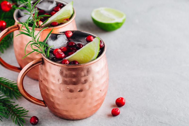 Two mugs of cranberry Moscow mules on a table with half a lime on a table and some cranberries