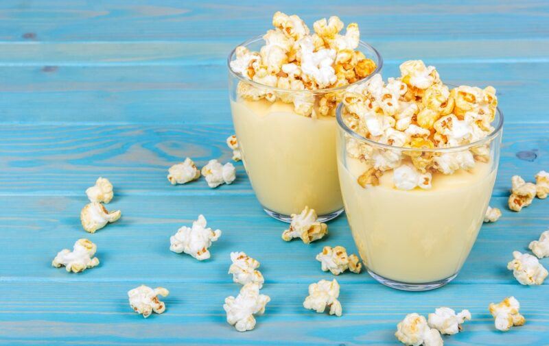 Two dessert glasses containing custard and creme brulee popcorn, with some more popcorn scatted on the table