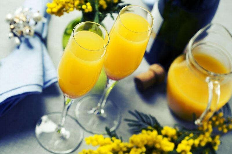 Two orange juice mimosas on a table next to a jug of orange juice