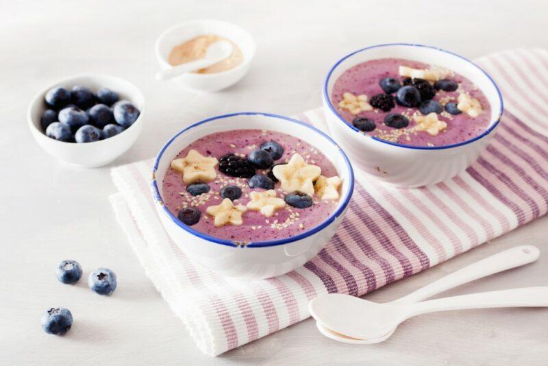 Two blue and white bowls with a berry smoothie, bananas, and blueberries