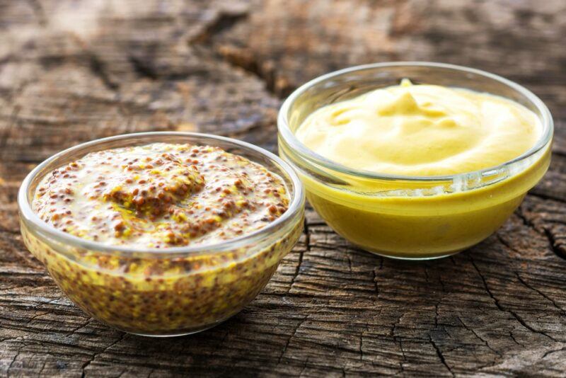 Two small glass dishes, one containing smooth mustard and the other containing mustard with seeds