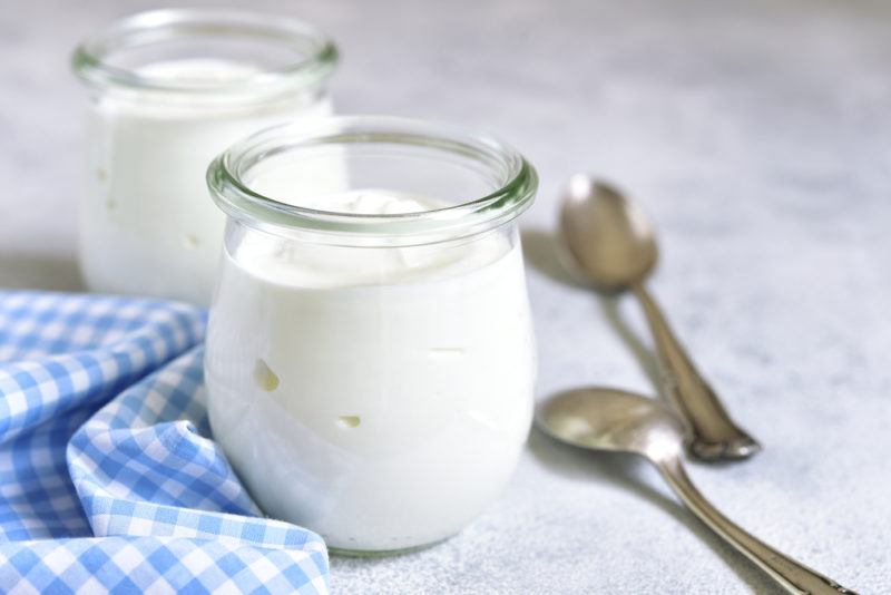 Two glass jars of yogurt next to a blue checkered cloth and two spoons