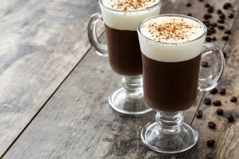 Two glasses containing Irish coffee on a wooden table surrounded by coffee beans