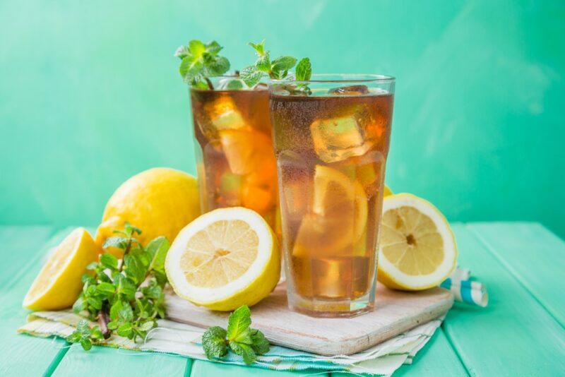 Two tall glasses containing a Long Island iced tea with lemons surrounding them