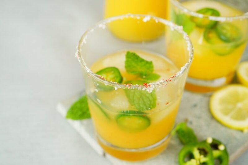 Two glasses containing a honey jalapeno whiskey and lemonade cocktail, with sugar or salt on the rim